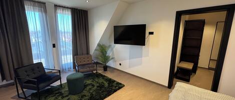 Una sala moderna con sofá, sillón, reposapiés y un televisor de pantalla plana montado en la pared.