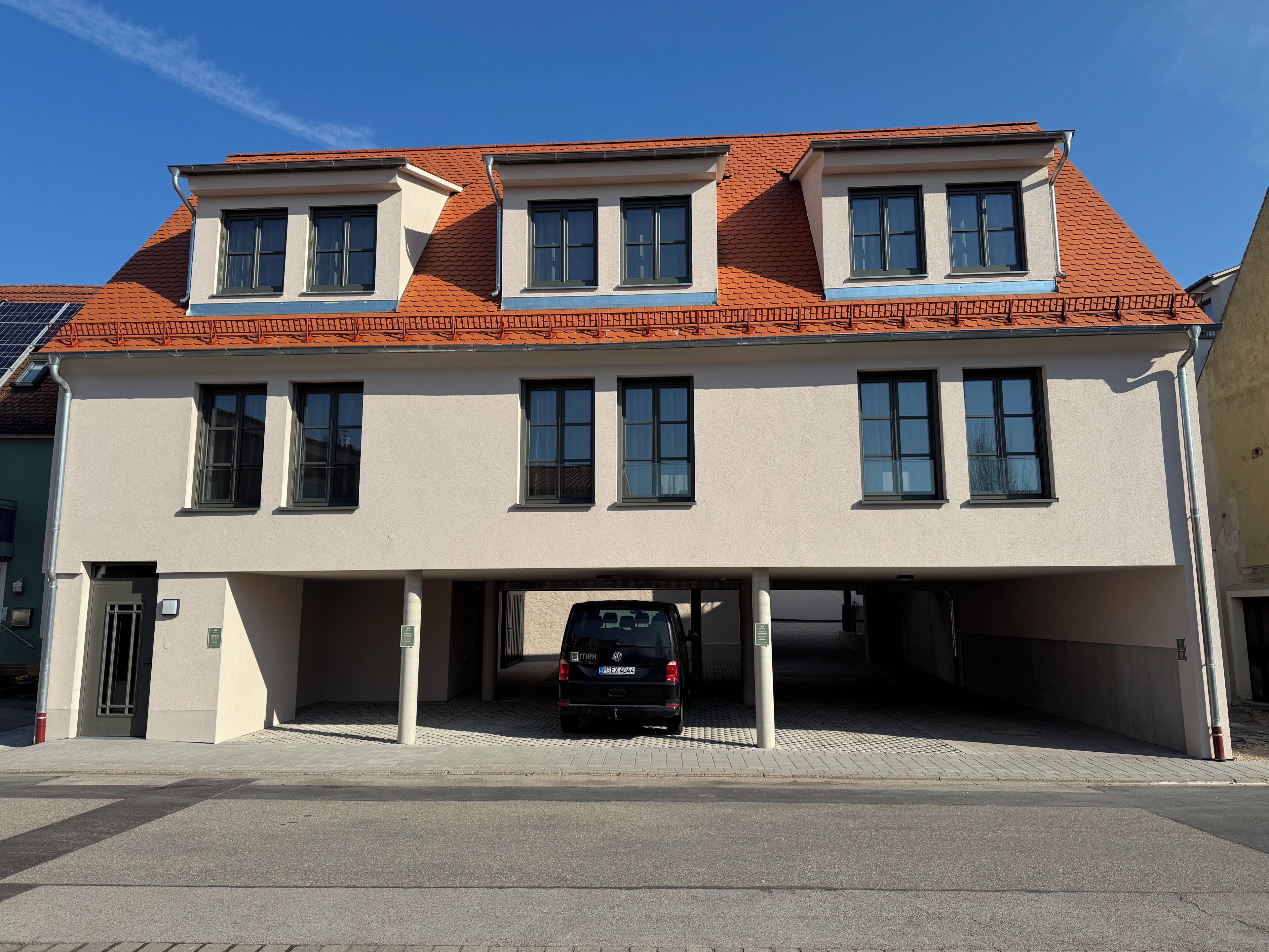 A two-story building with a red-tiled roof, multiple windows, and a parking garage.