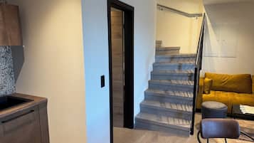 A modern interior with a kitchen, a staircase, and a living area with a sofa and ottoman.