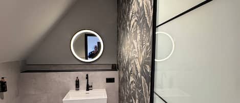 A modern bathroom with a white sink, black towel rack, and a mirror with a circular light.
