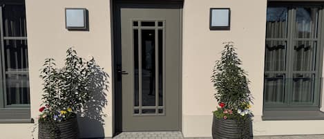 Un edificio con una puerta oscura, dos macetas con flores y ventanas con persianas.
