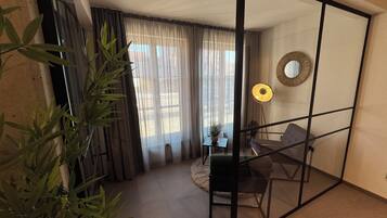 Una habitación moderna con separador de vidrio, una mesa de comedor, sillas, una pequeña planta en maceta, una lámpara de pie y un espejo en la pared.