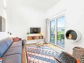 Ein modernes Wohnzimmer mit einer Couch, einem Fernseher, einem Kamin und einem großen Fenster.