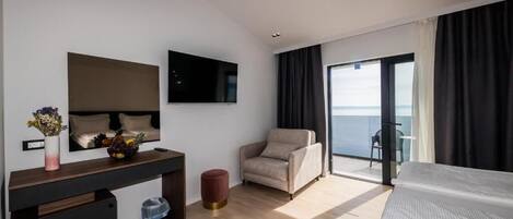 Et moderne hotelværelse med en seng, et skrivebord med blomster i en vase, en stol og et stort vindue med havudsigt.