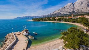 A coastal town with a marina, clear blue waters, and a mountain backdrop. - Villa Marello (Promajna)