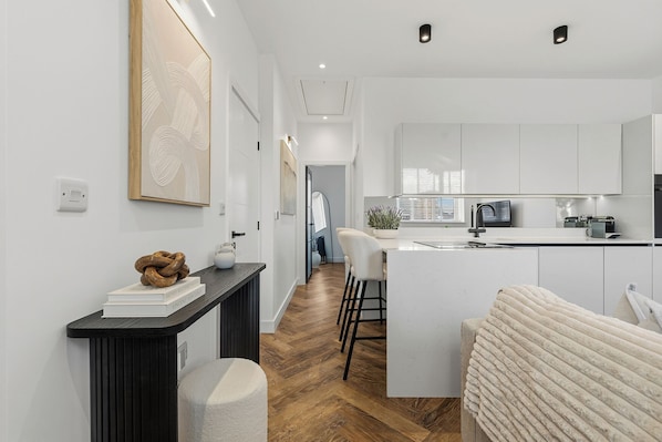 A modern kitchen with white cabinets, a central island, and a dining area with a white chair.