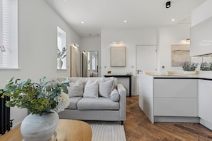 A modern living room with a grey sofa, a wooden coffee table, and a large vase with flowers.