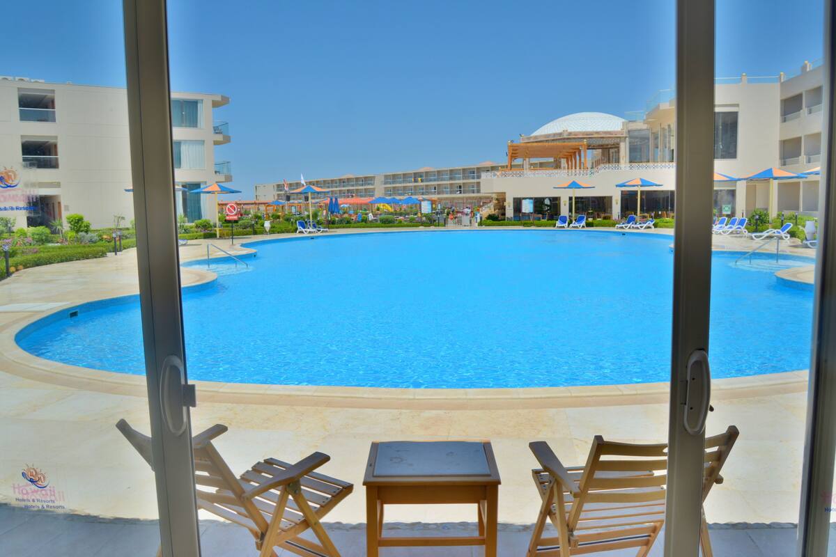 A pool area with lounge chairs and a table, surrounded by a building with multiple floors and balconies.