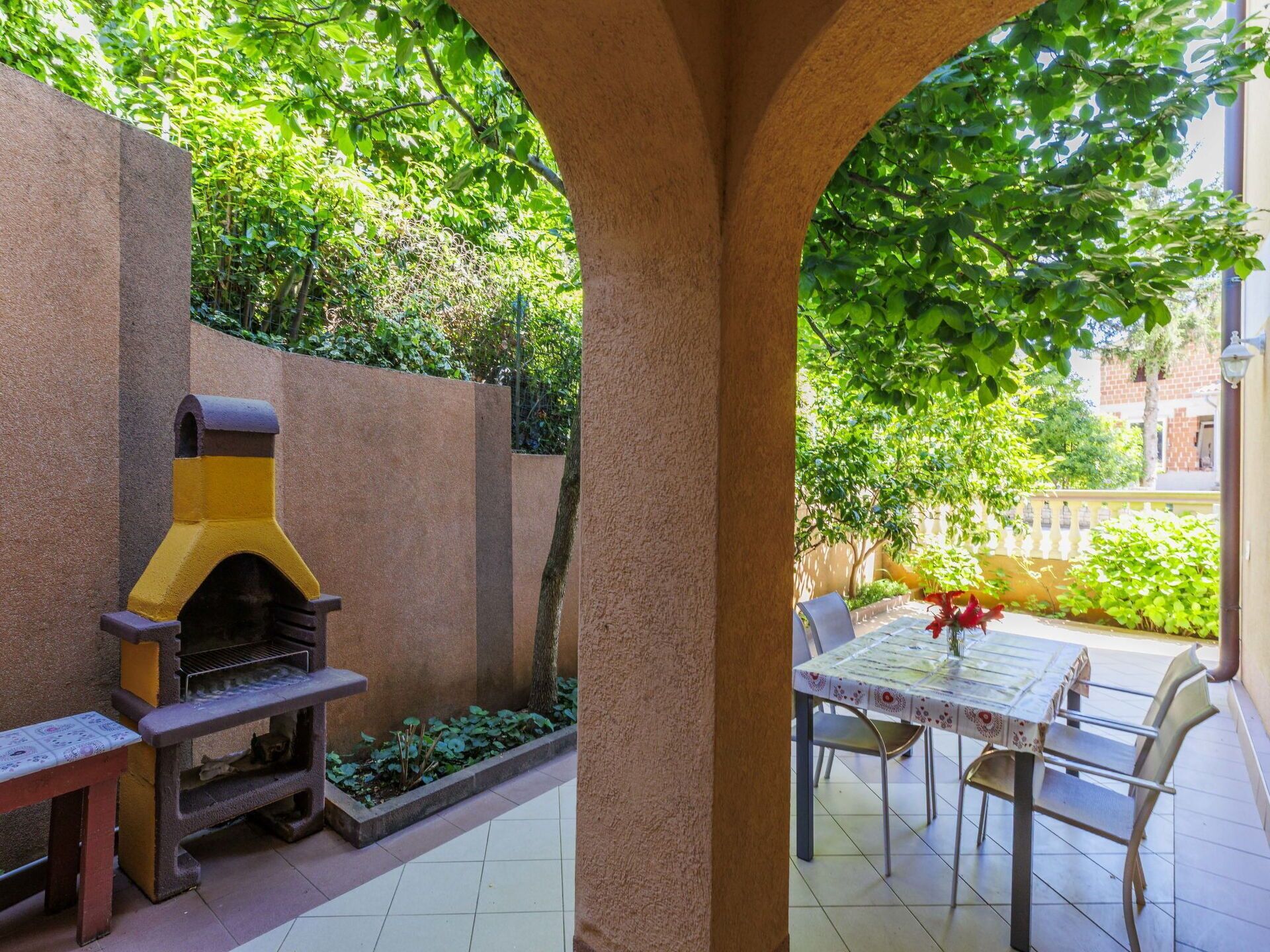 Un patio exterior con una parrilla, una mesa y sillas, y vistas a zonas verdes y edificios.