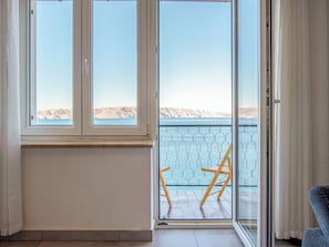 Ein Zimmer mit großem Fenster, einer Schiebetür zum Balkon mit einem Stuhl und Blick auf eine Berglandschaft.