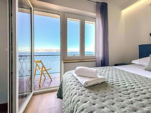 Ein Schlafzimmer mit Bett, Sessel und Meerblick durch große Fenster.