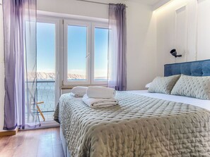Ein Schlafzimmer mit Bett, Kopfstütze, einem Fenster mit Vorhängen und Blick auf eine Berglandschaft.
