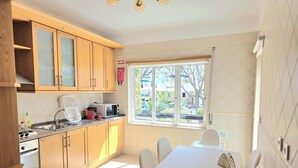 Una cocina con armarios de madera, microondas, hervidor y ventana con vistas al exterior.
