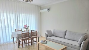 Una sala de estar con sofá, una mesa de centro, una mesa de comedor con sillas y un jarrón de flores.
