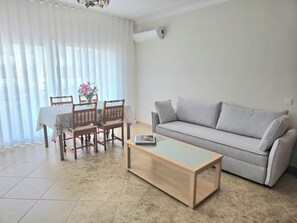 A living room with a sofa, a coffee table, a dining table with chairs, and a flower vase. - Blue Diamond Peaceful Apartment II Tavira (Tavira)