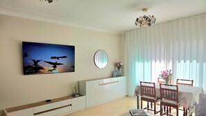 Una sala de estar moderna con un televisor de pantalla plana, un espejo redondo, una mesa de comedor con sillas y un sofá.