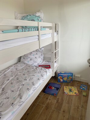 A bunk bed with a white and teal patterned bedspread, a red book, and a Kinder Spiele board game on the floor.