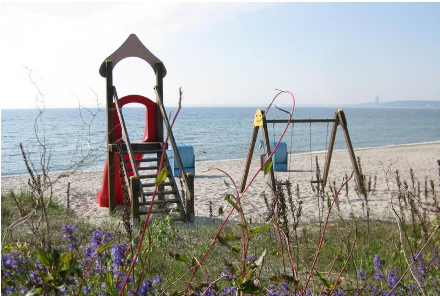 Une plage avec des balançoires et un toboggan, entourée de végétation.