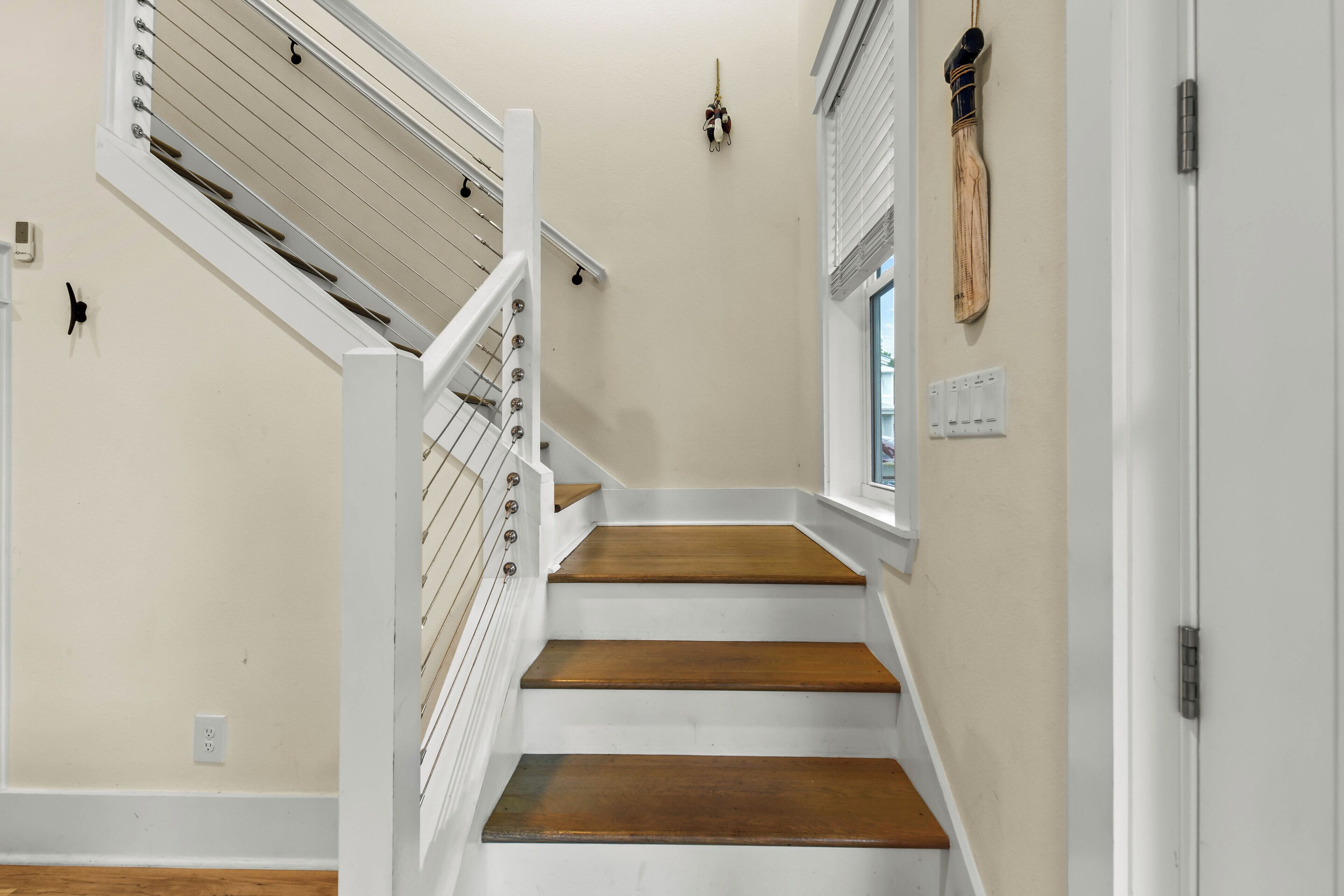 Un escalier avec des rampes blanches et des marches en bois, un luminaire fixé au mur et une porte dotée d’une fenêtre.