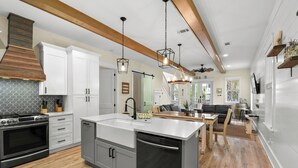 A modern kitchen with white cabinets, a stainless steel stove, and a central island with a sink. - Retreat at 30A (Santa Rosa Beach)
