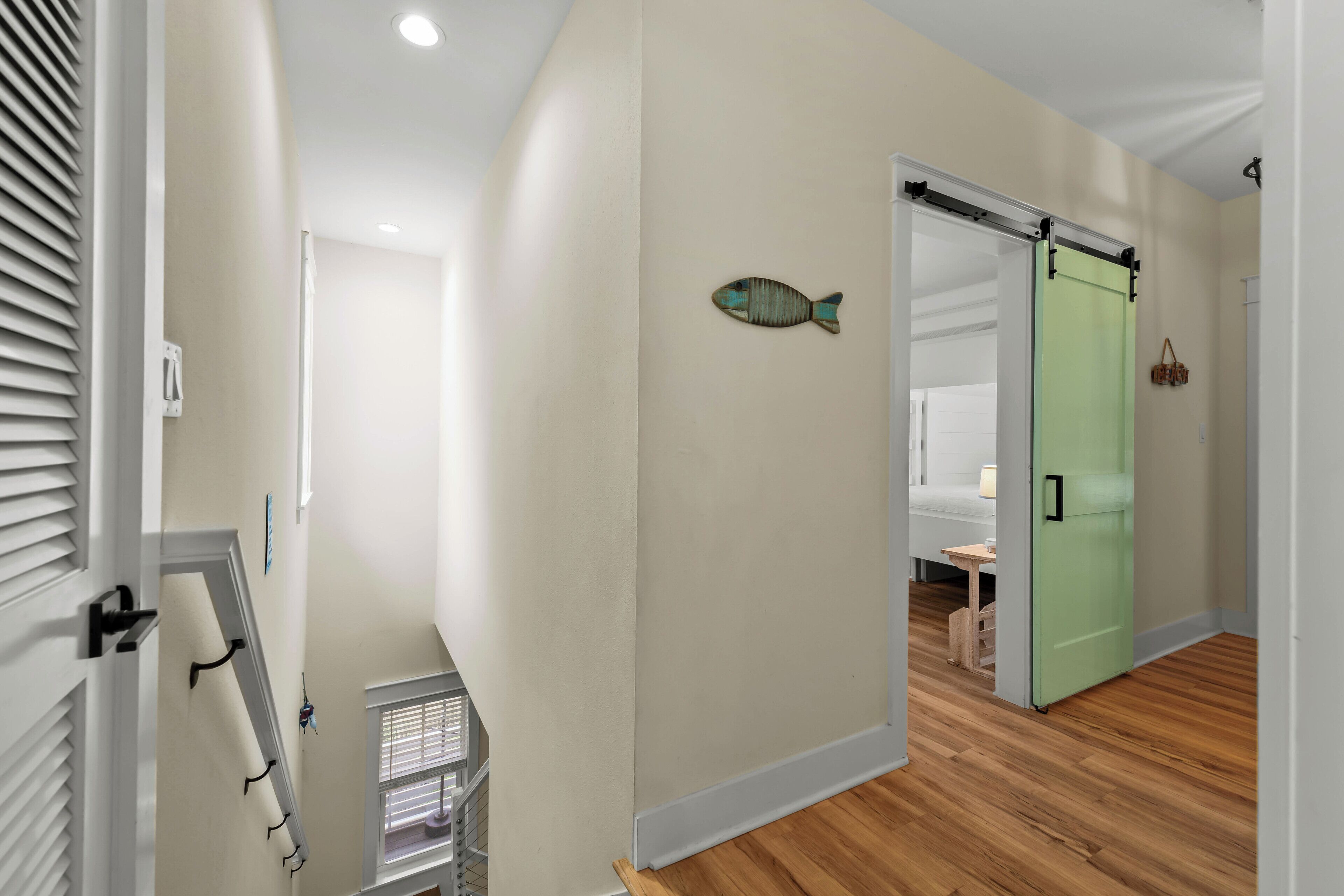 A hallway with a wooden floor, a green door, and a fish decoration on the wall.