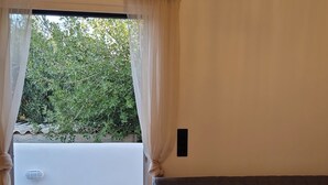 A room with a sofa, a small table, and a view of greenery outside. - Alya Paros – Calm Cycladic Aesthetic (Paroikia)