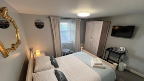Ein Hotelzimmer mit einem Bett, einem Fernseher, einem Kleiderschrank und einem Schreibtisch mit Wasserkocher.