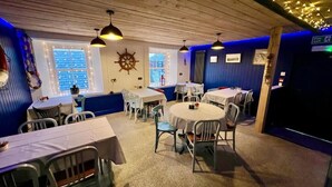 Ein Restaurant mit runden Tischen und Stühlen, Holzbalkendecke und Lichterketten.