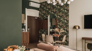 A modern living room with a sofa, a dining table with chairs, a TV, and a decorative wall. - White Lotus by Fragola Apartments (Kraków)