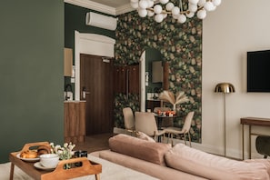A modern living room with a sofa, a dining table with chairs, a TV, and a decorative wall. - White Lotus by Fragola Apartments (Kraków)