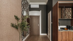 A hallway with a wooden floor, a potted plant, a door, and a kitchen area with a coffee maker and fruit. - White Lotus by Fragola Apartments (Kraków)