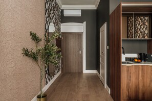 A hallway with a wooden floor, a potted plant, a door, and a kitchen area with a coffee maker and fruit. - White Lotus by Fragola Apartments (Kraków)
