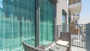 Een balkon met rieten meubels, een glazen wand en uitzicht op een modern gebouw.