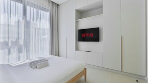 Een moderne hotelkamer met een bed, een aan de muur bevestigde televisie en een raam met dunne gordijnen.
