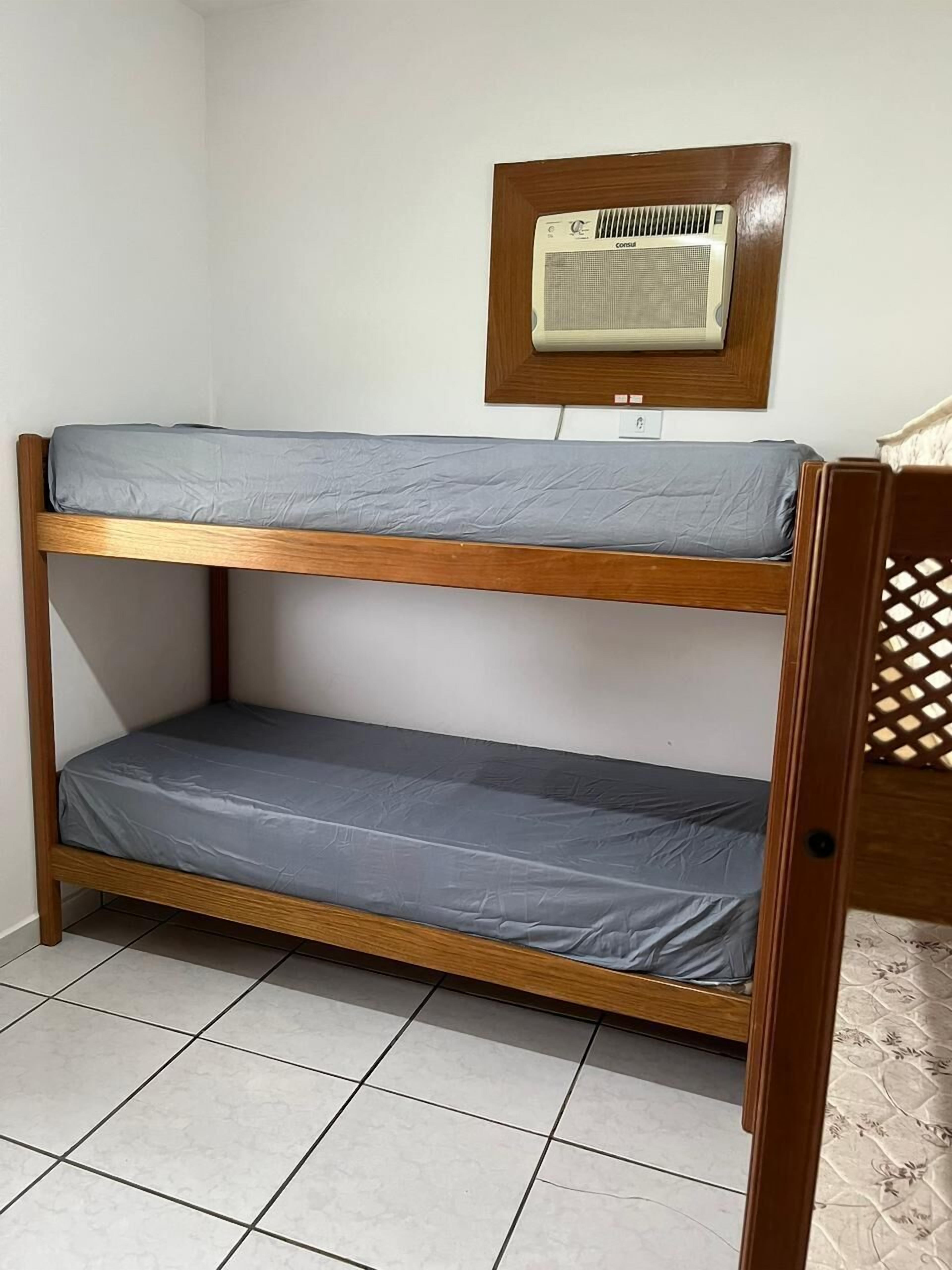 A bunk bed with grey bedding, a wooden frame, and a wall-mounted air conditioner above it.