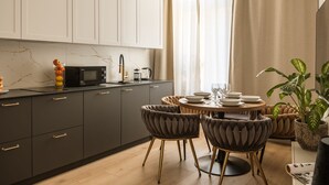 Une cuisine moderne avec des meubles de couleur sombre, un pare-feu en marbre et un coin repas doté de tables rondes et de chaises rembourrées.
