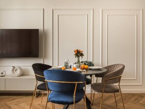 Ein Essbereich mit einem runden Tisch, vier Stühlen, einer Blumenvase und einem an der Wand befestigten Flachbildfernseher.