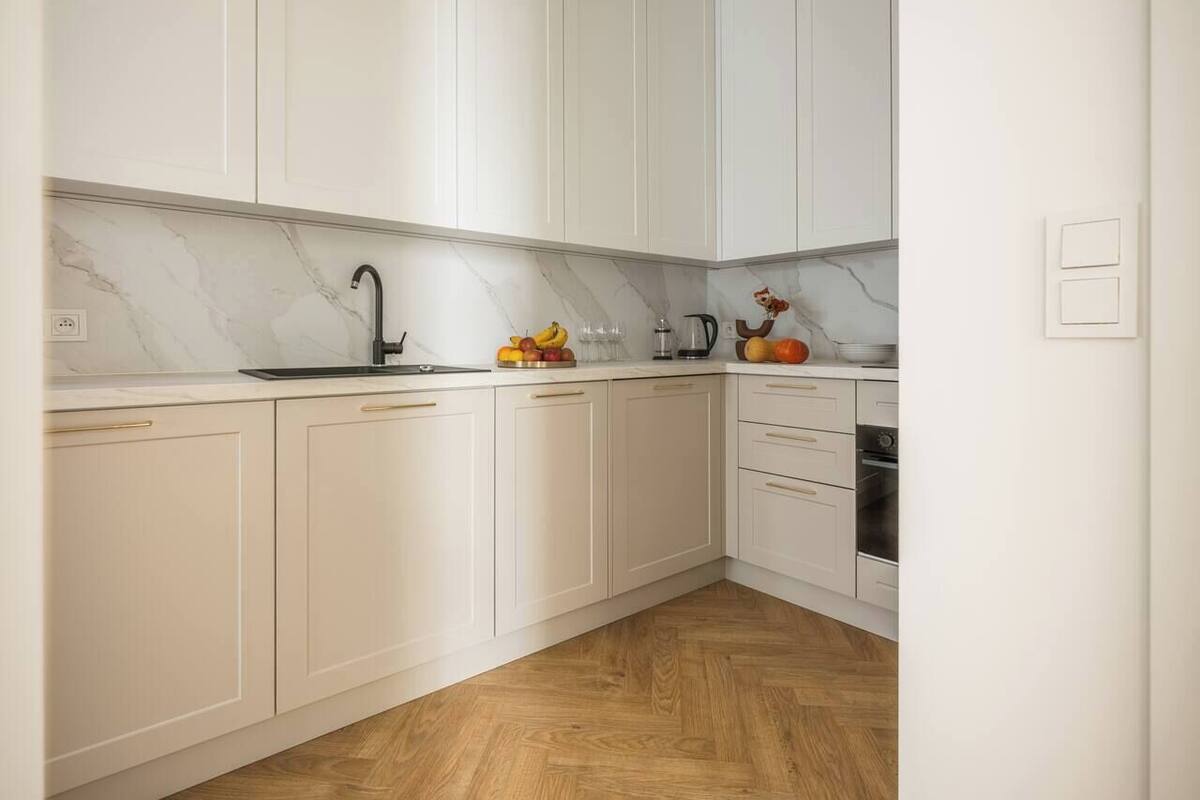 A kitchen with white cabinets, a marble countertop, and a wooden floor.