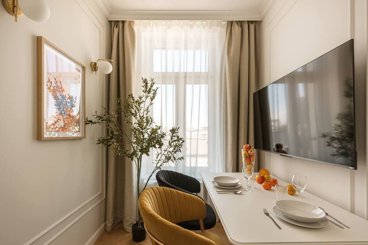 Een eethoek met een gedekte tafel voor twee personen, een potplant en een flatscreen televisie aan de muur.