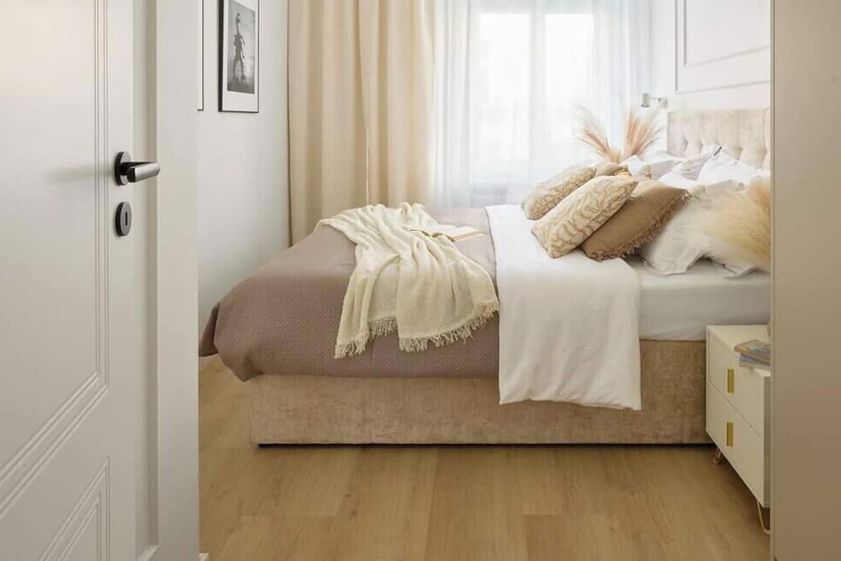 Een slaapkamer met een bed, nachtkastje, kledingkast en een raam met gordijnen.