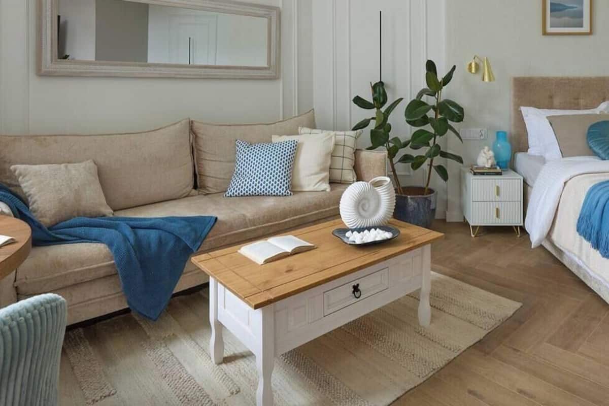 Een goed verlichte kamer met een bank, een bed, een klein tafeltje met een boek en een schaal chocolade, een nachtkastje en een potplant.