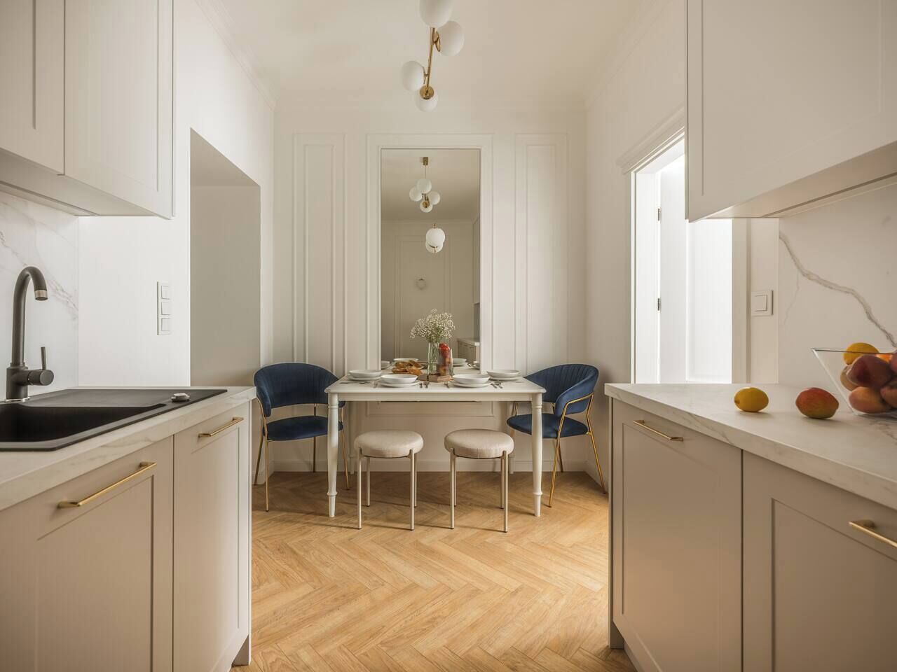 Eine moderne Küche mit weißen Schränken, einer schwarzen Spüle und einem Essbereich mit zwei Stühlen und einem Tisch.