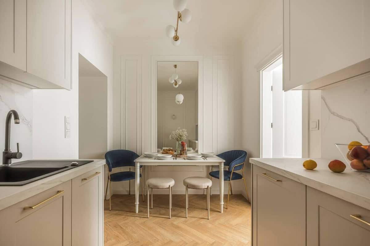 Een moderne keuken met witte kasten, een zwarte spoelbak en een eethoek met twee stoelen en een tafel.