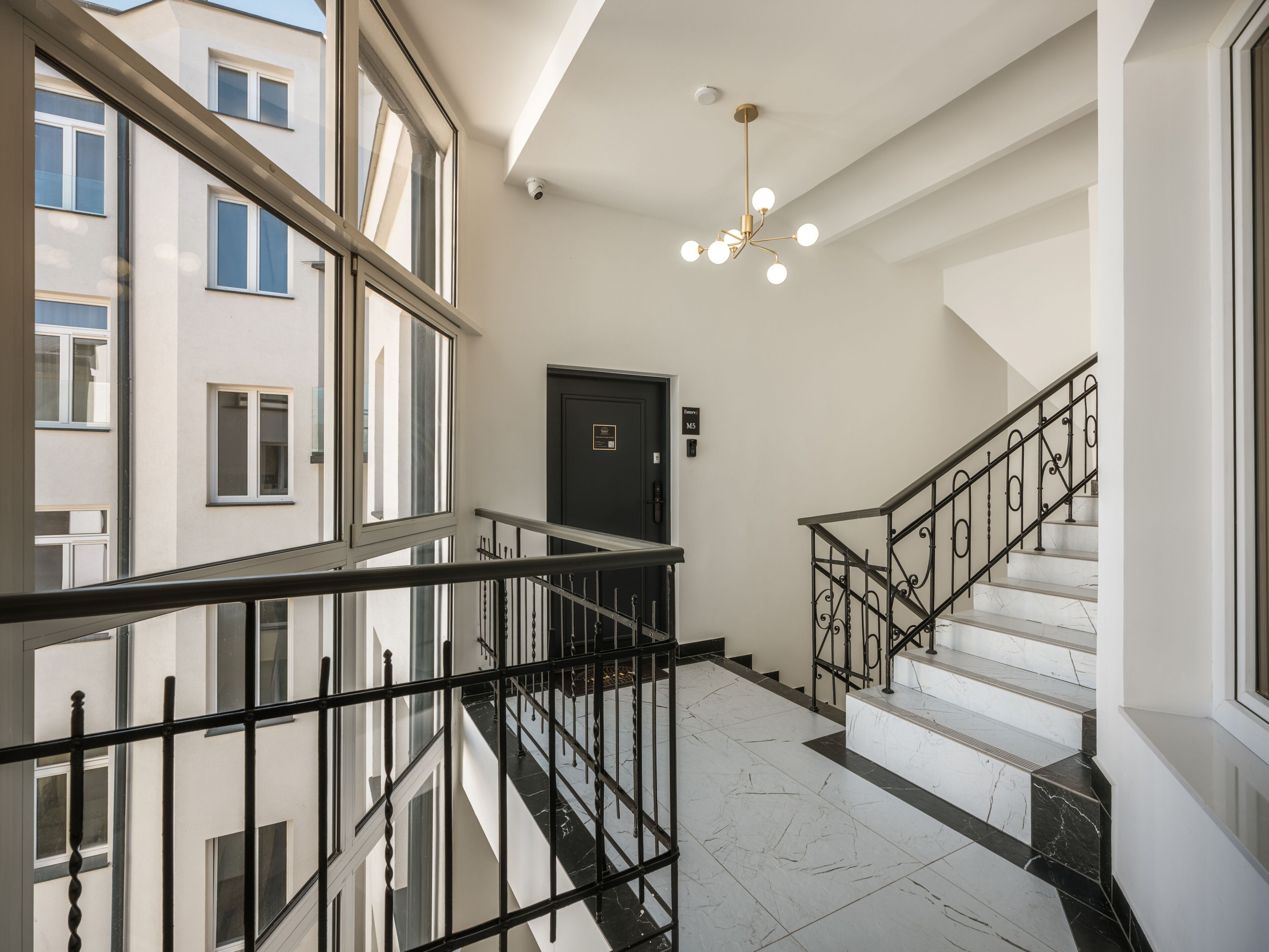 A modern interior with a staircase, a black door, and a security camera on the ceiling.
