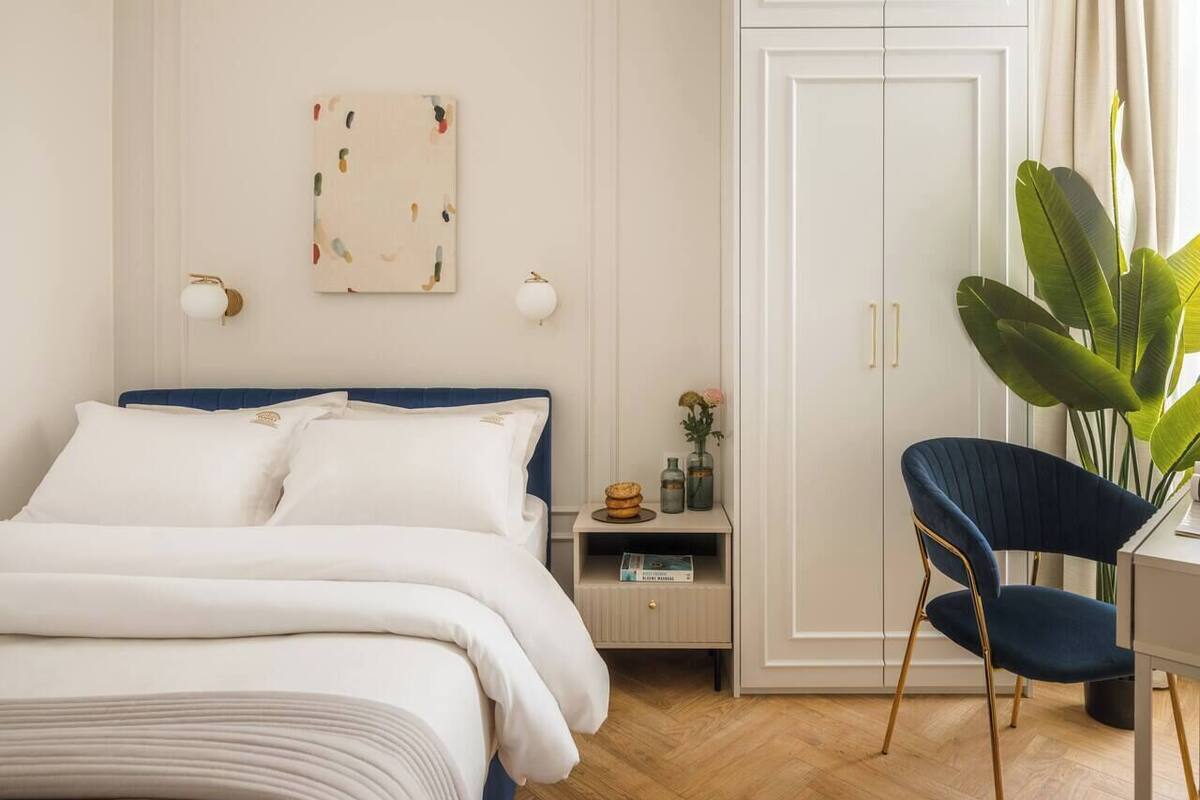 Een slaapkamer met een bed, nachtkastje, lamp, stoel en kledingkast.