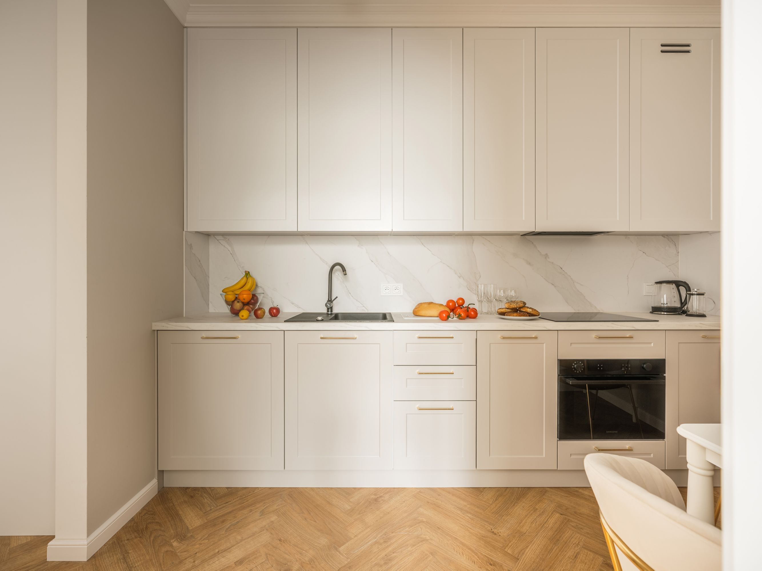 A modern kitchen with white cabinets, a marble backsplash, and a built-in oven.
