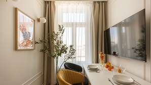 Un coin repas avec une table dressée pour deux personnes, une plante en pot et une œuvre d’art encadrée accrochée au mur.