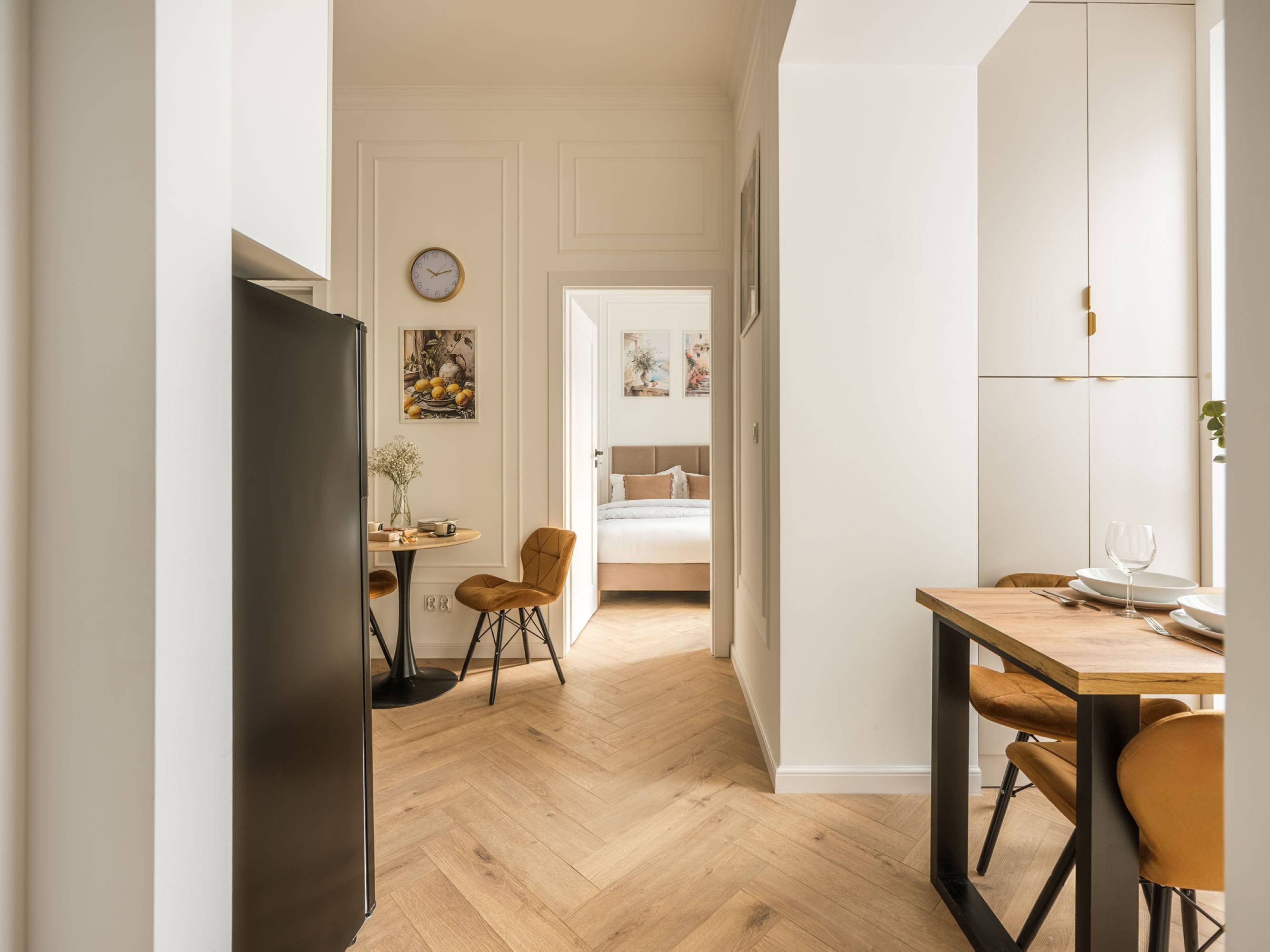 Una cocina moderna con suelo de madera, una zona de comedor con mesa y sillas, y un dormitorio con cama y mesita de noche.
