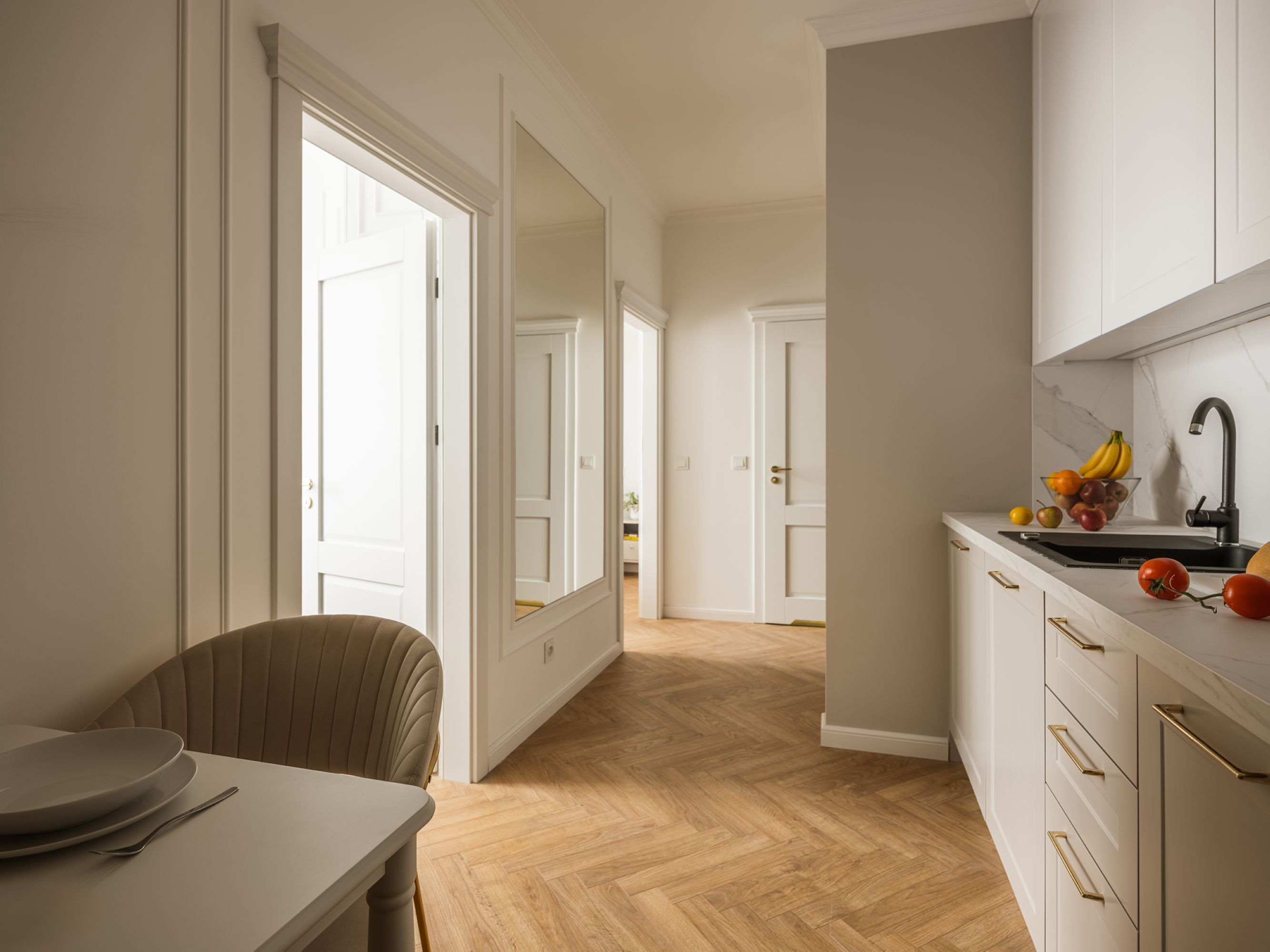 A modern kitchen with a wooden herringbone floor, white cabinetry, and a black faucet.