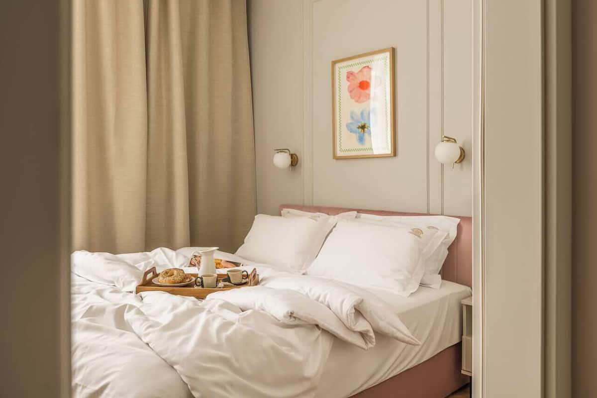 A neatly made bed with pillows and a tray of breakfast items, a framed floral artwork on the wall, and a light fixture.